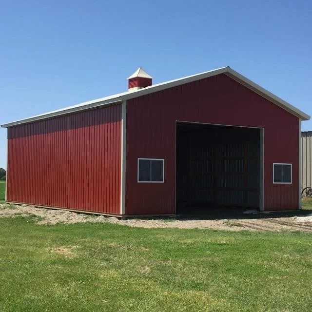Red barn with open front on a grassy field under a clear blue sky