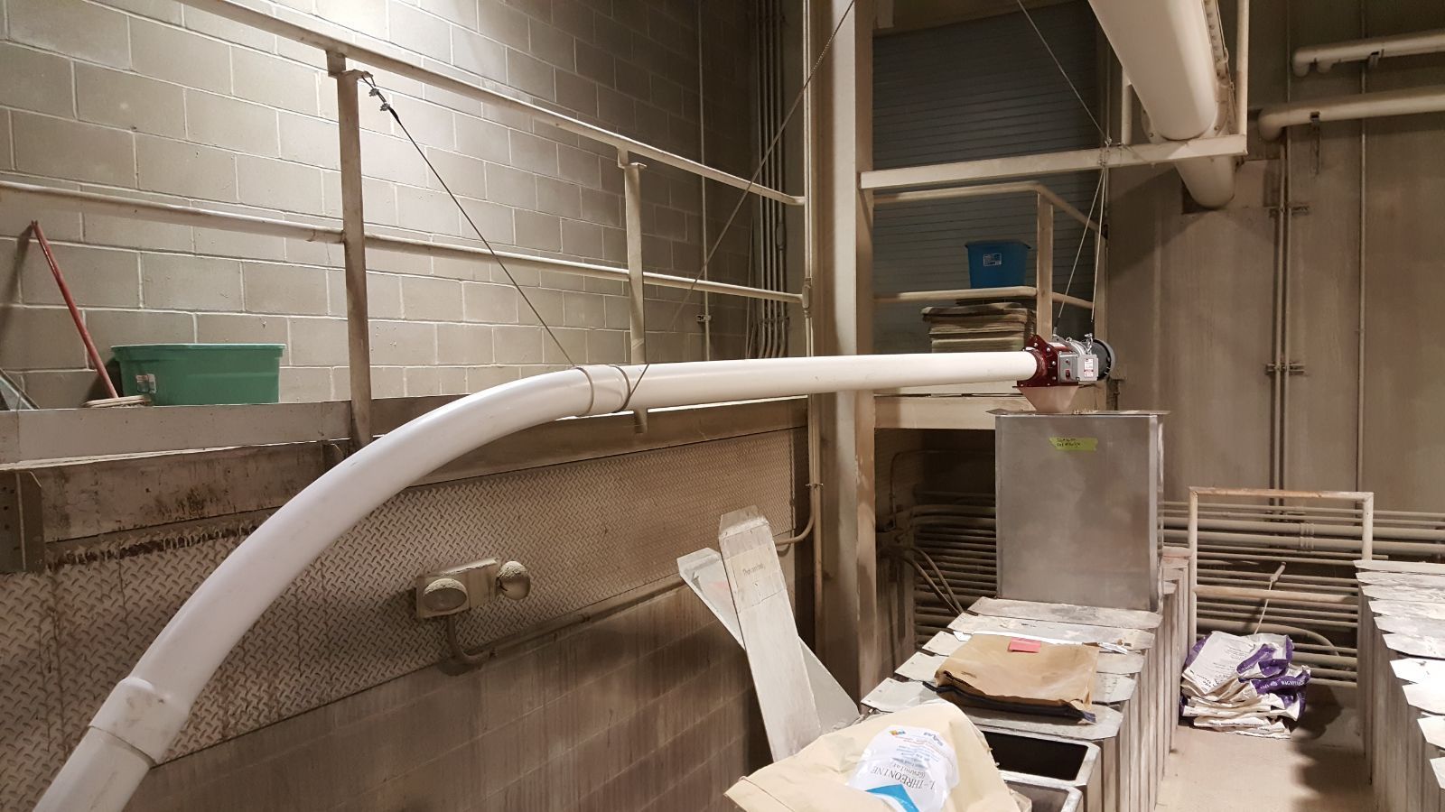 Industrial room with a large white pipe, metal shelving, and scattered equipment on the floor.