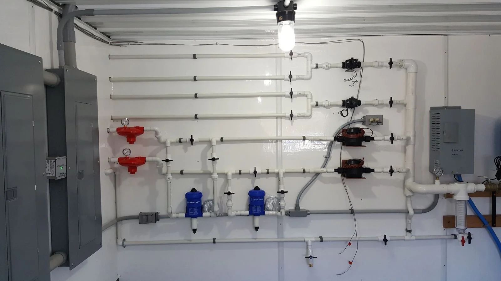 Industrial wall with pipes, valves, meters, and electrical panels in a utility room