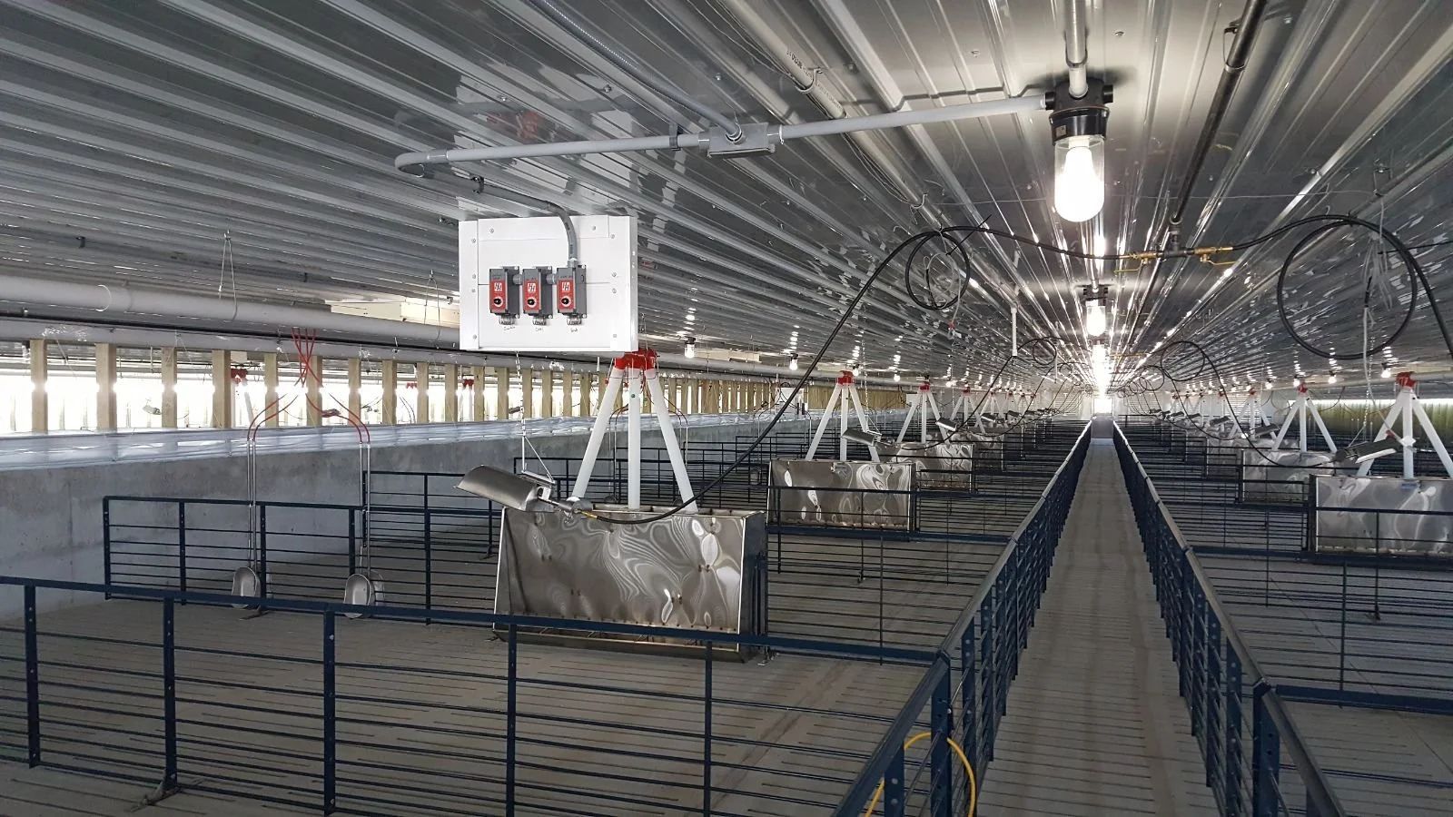 Indoor industrial facility with metal catwalks, fencing, and a hanging digital display overhead