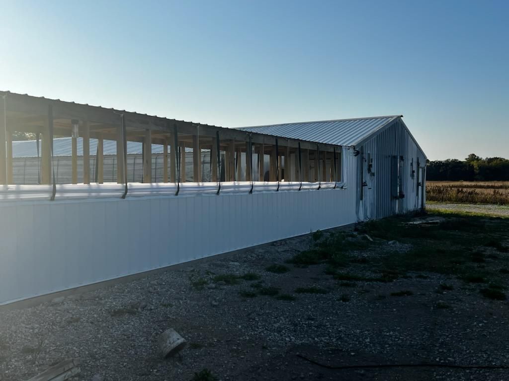 Long white industrial building with windows, lit by low sun on a gravel lot