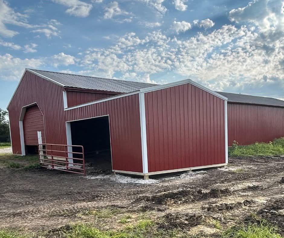 Red barn with open doorway and metal gate on a muddy farm under a cloudy sky.