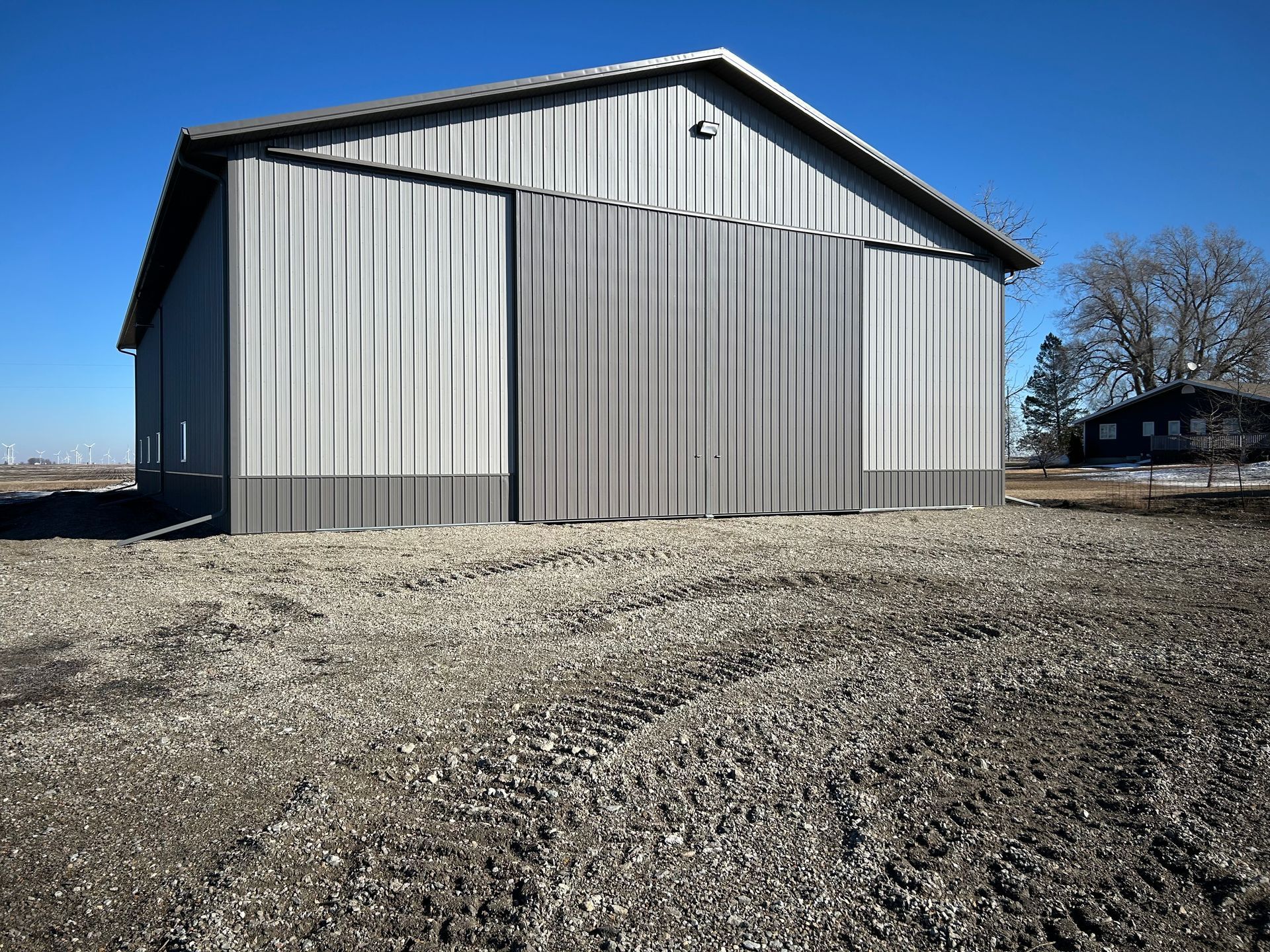 Gray metal barn on a gravel lot under a clear blue sky
