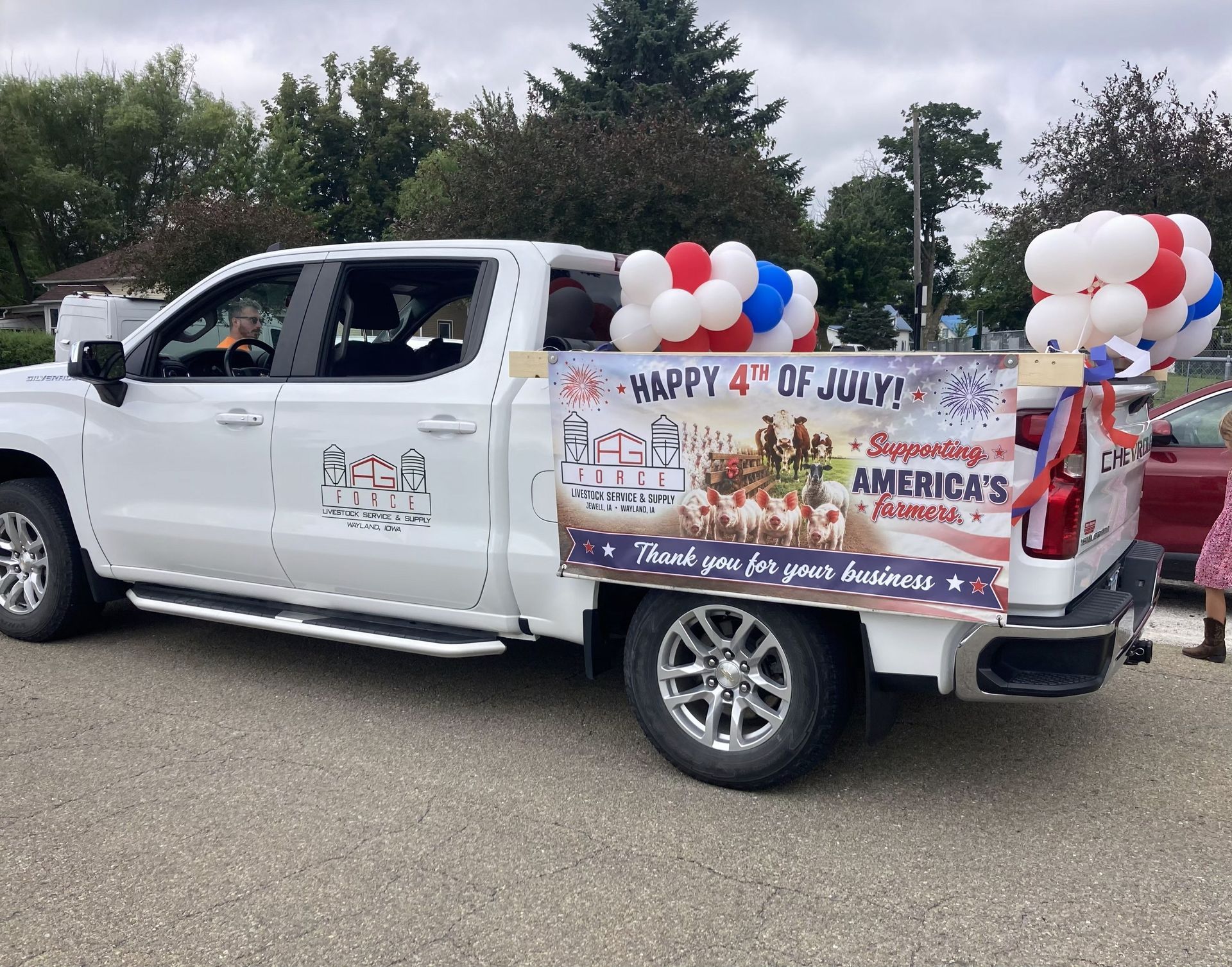 White pickup truck decorated for a July 4th parade with red, white, and blue balloons and a patriotic banner