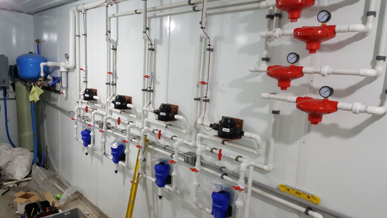 Industrial piping system with white pipes, blue valves, and red gauges along a wall