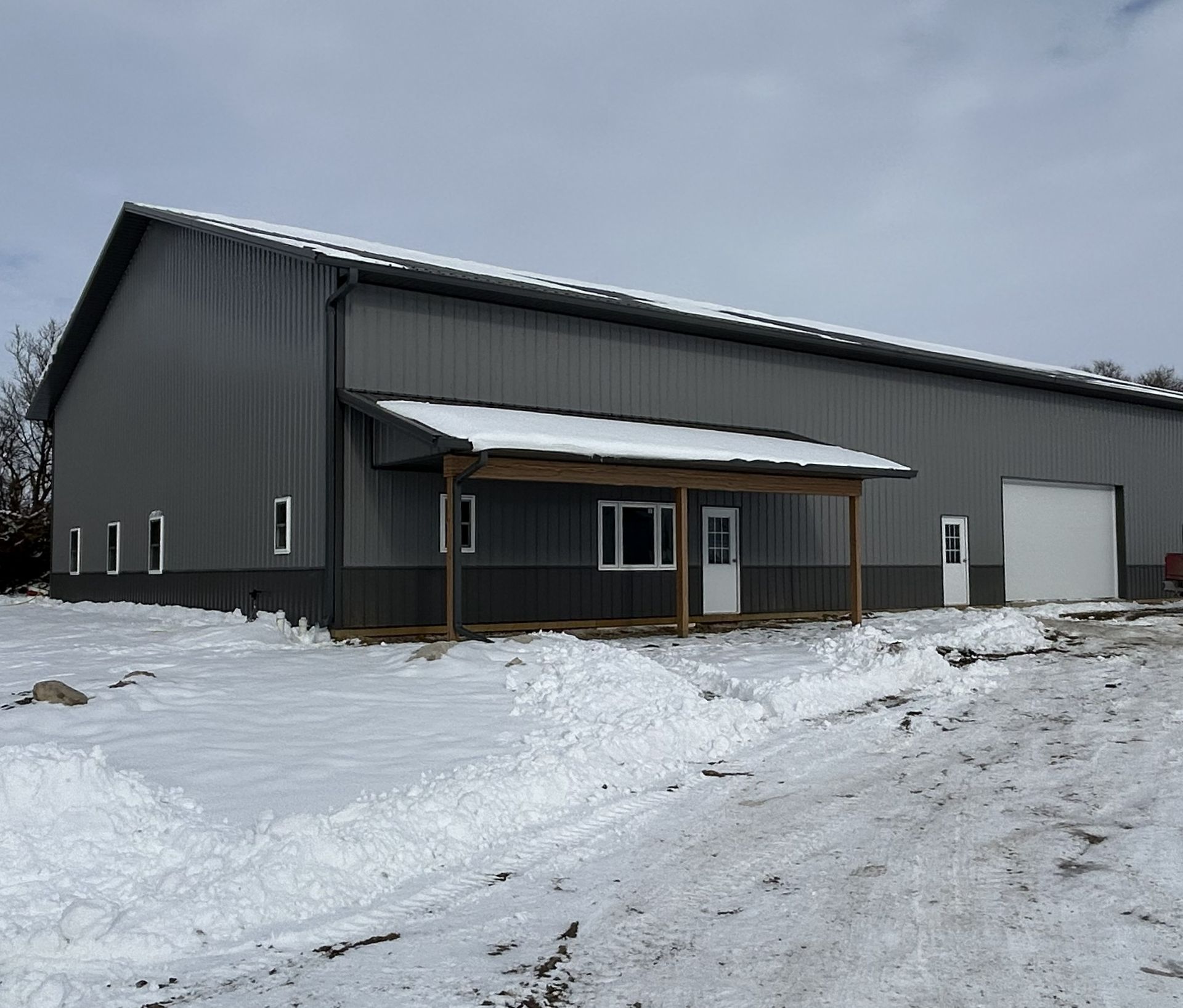 Long dark grey metal building with a covered entrance porch surrounded by a snow-covered ground.