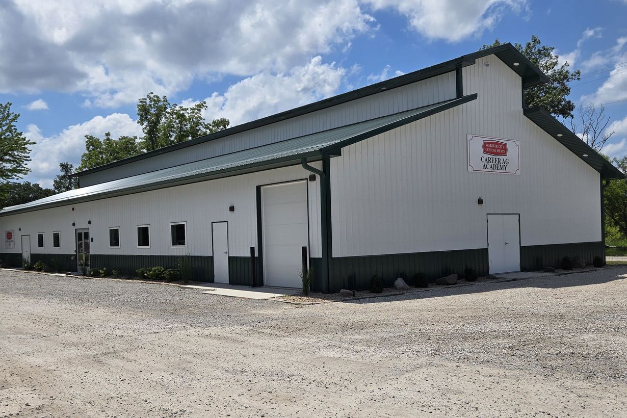White industrial warehouse with green trim on a gravel lot under a partly cloudy sky