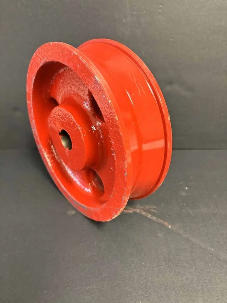 Red metal pulley wheel with a grooved rim on a dark surface