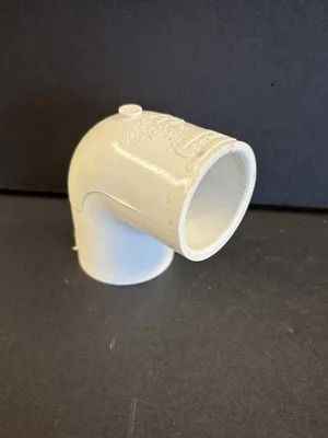 White plastic 90-degree pipe elbow fitting on a dark surface against a dark background