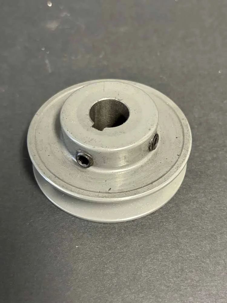 Silver metal pulley with a central hole and set screw on a dark surface