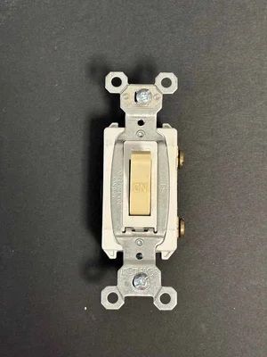 A white electrical wall switch with a beige toggle on a black background.