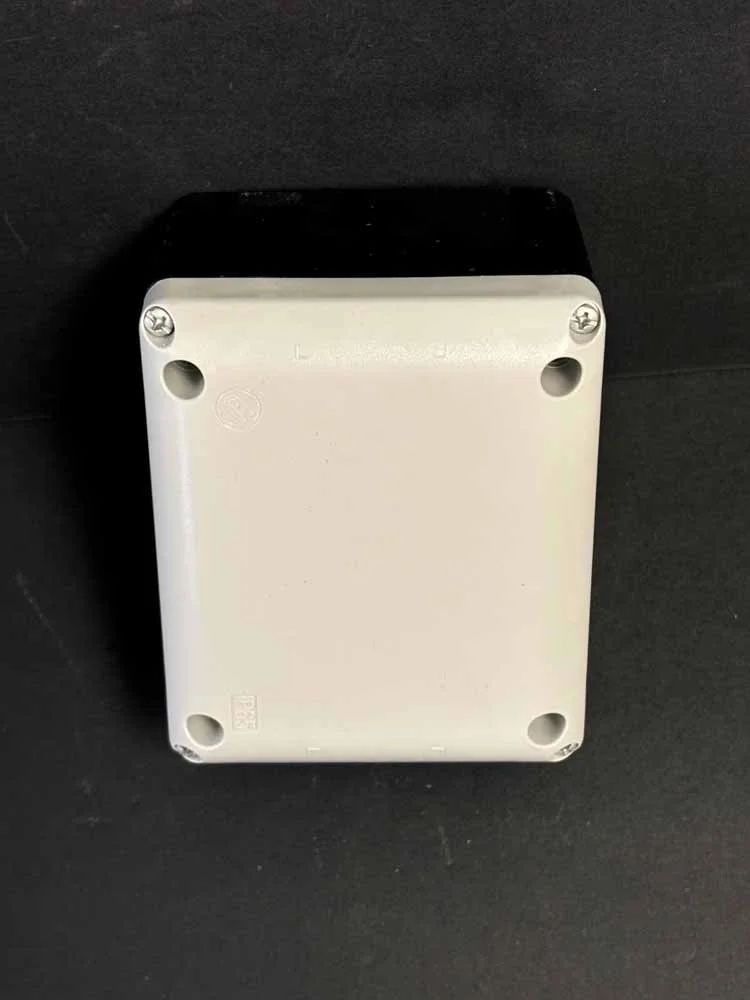 White rectangular electrical enclosure with four corner screws on a black background