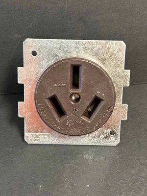 Brown electrical wall socket on a silver metal plate against a dark background