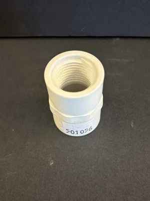 White plastic threaded pipe fitting on a black surface, with a small label number printed near the base.