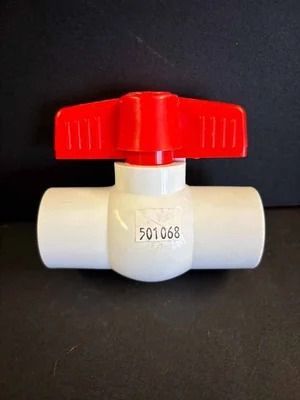 White plastic ball valve with a red handle on a dark background.