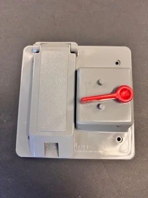 Gray electrical switch box with a red lever on a dark surface