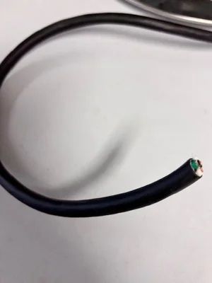 Black electrical cable with exposed copper wire at the cut end on a light surface
