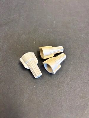 Three small beige plastic cable nuts on a dark gray surface