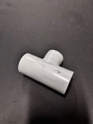 Small white plastic T-shaped pipe fitting on a dark surface