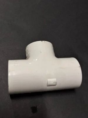 White PVC T-fitting connector on a dark surface.