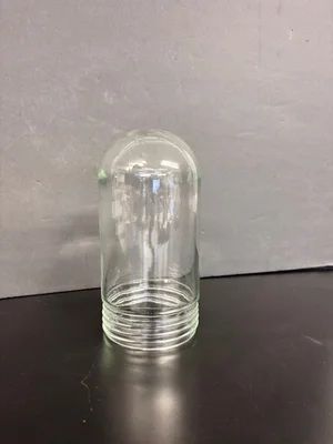Clear glass bottle standing upright on a black surface against a gray wall.