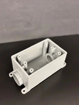 White plastic electrical junction box with mounting ears and internal standoffs on a gray surface