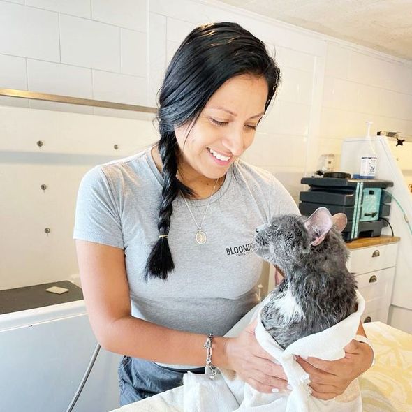 Woman holding a small dog in a white outfit, both smiling in a bright room