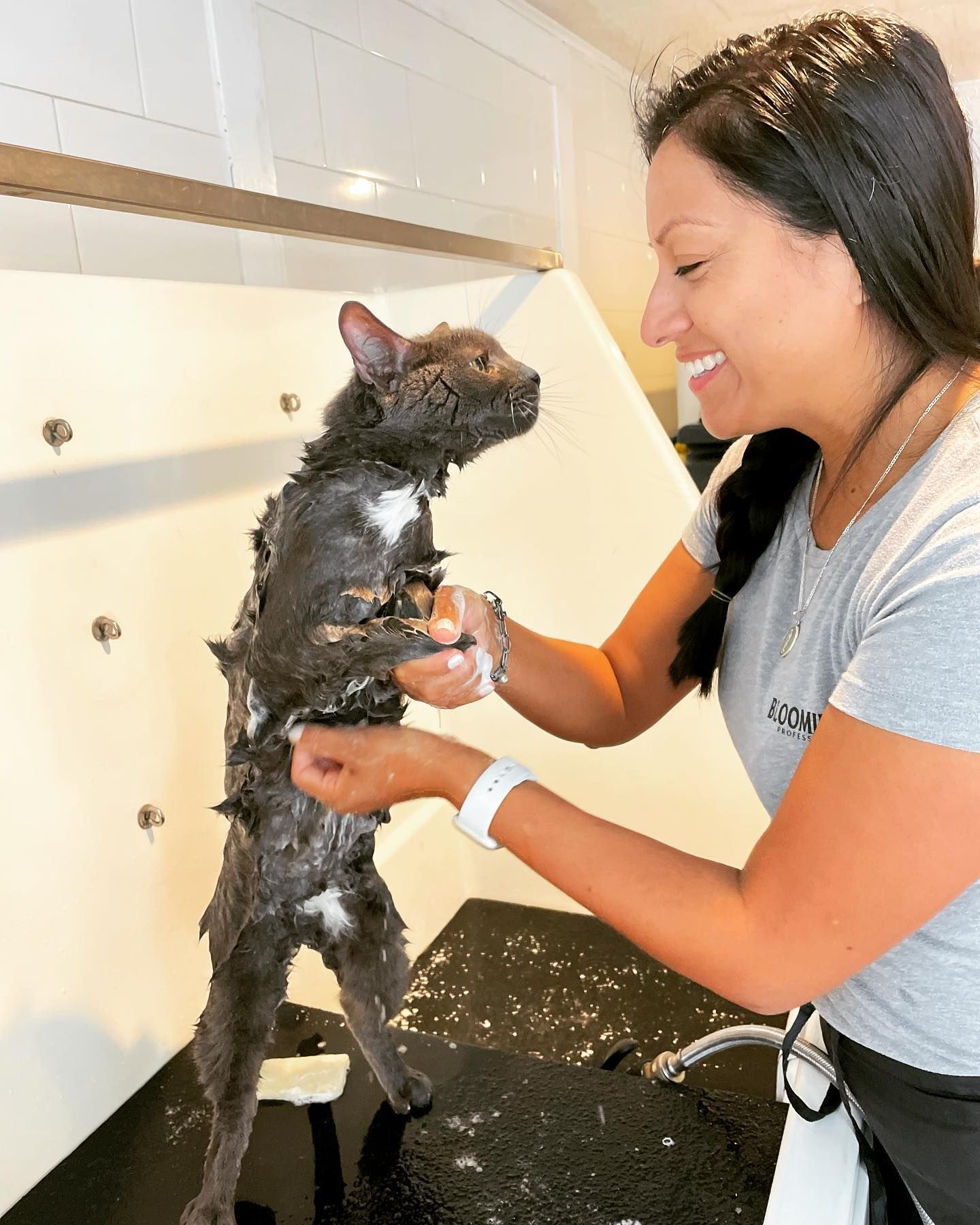 Woman bathing a small black cat in a sink, gently holding it under running water