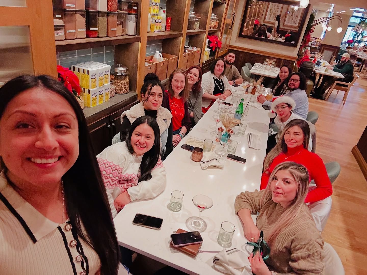 Group of people smiling around a long table in a cozy restaurant, taking a selfie.