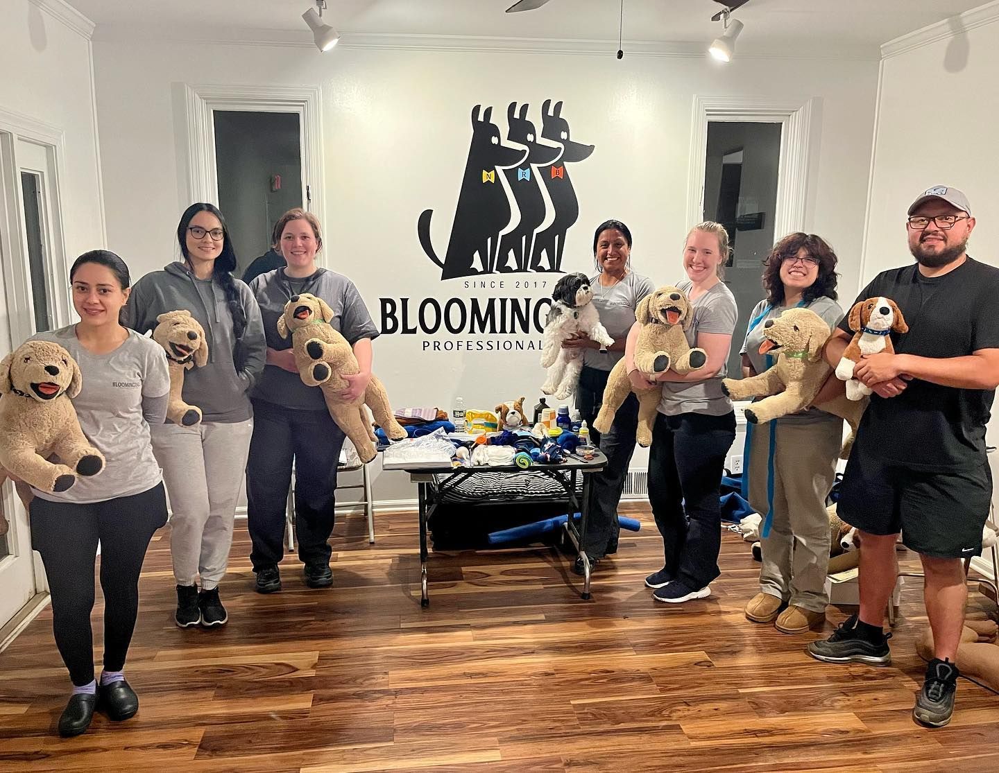 Group holding dogs in a pet grooming studio with a Blooming Pets sign on the wall