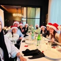 A group of people wearing Santa hats smile while sitting around a dinner table at a restaurant.