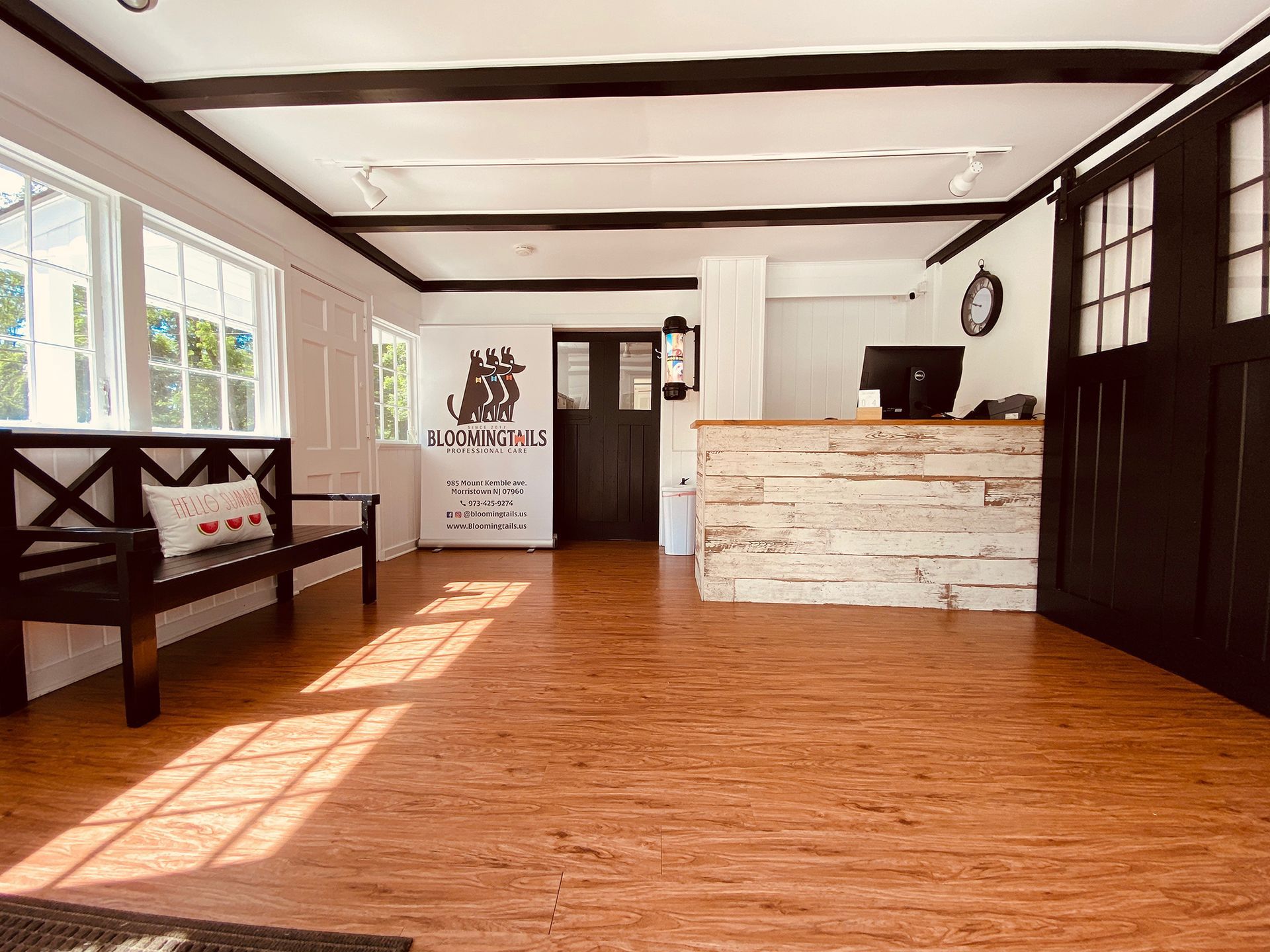 Bright modern living room with wood floors, white walls, black bench, and rustic reception desk