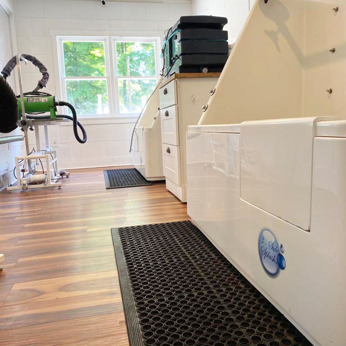 Laundry room with stacked washers, wood floor, window, and cleaning equipment area