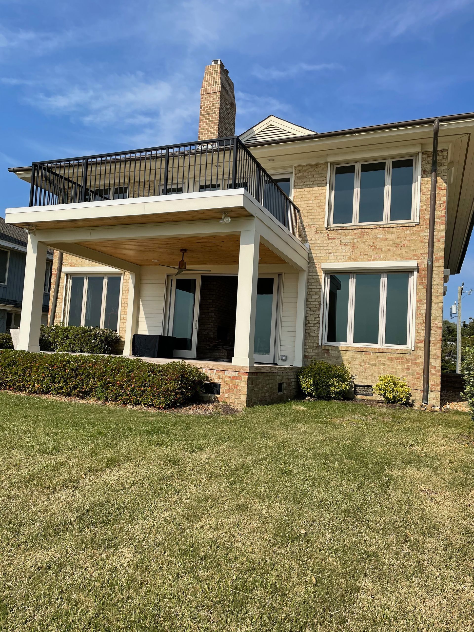 Two-story brick house with porch, balcony, and grass lawn under a blue sky.