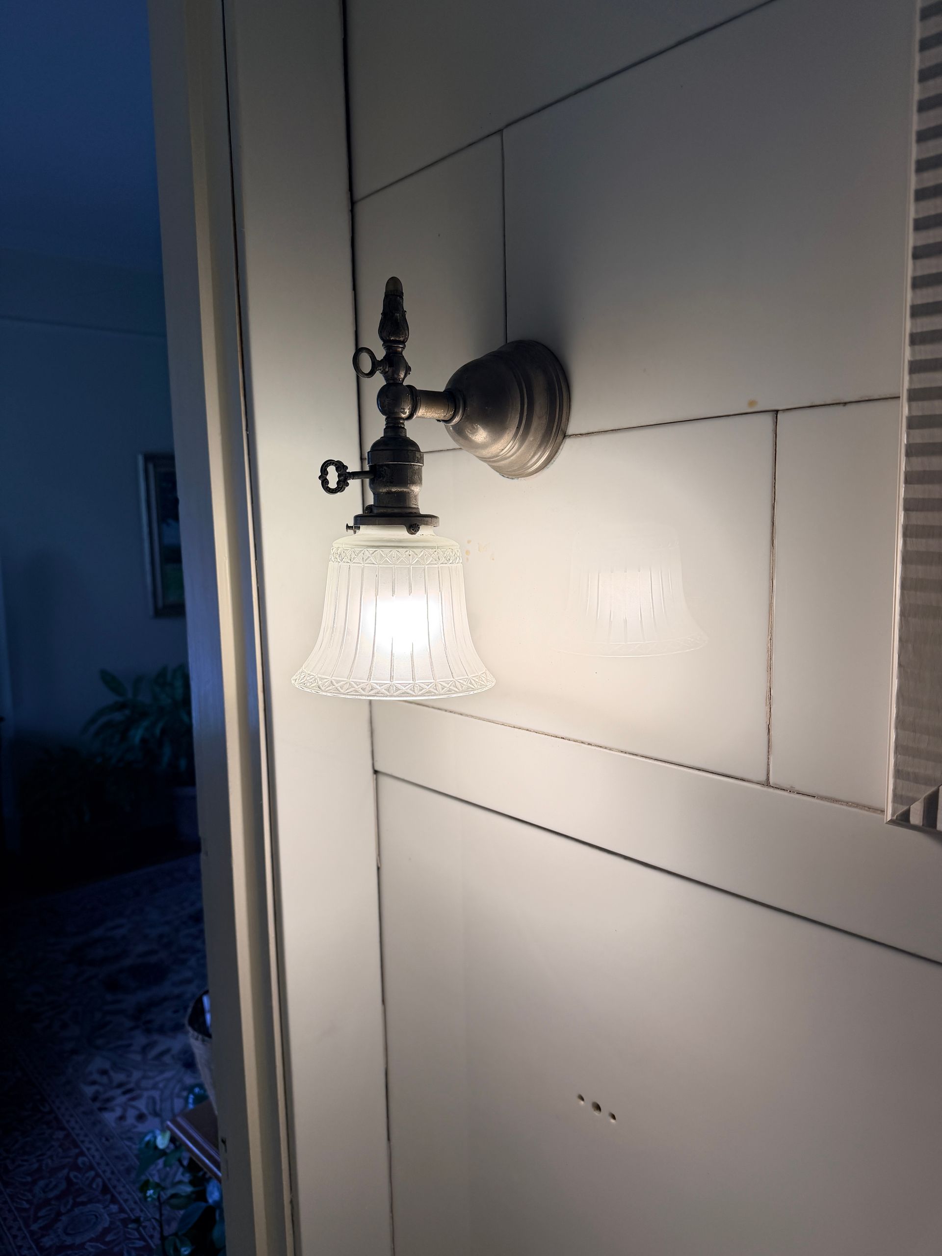 Wall-mounted porch light with a frosted glass shade shining beside a white door at night