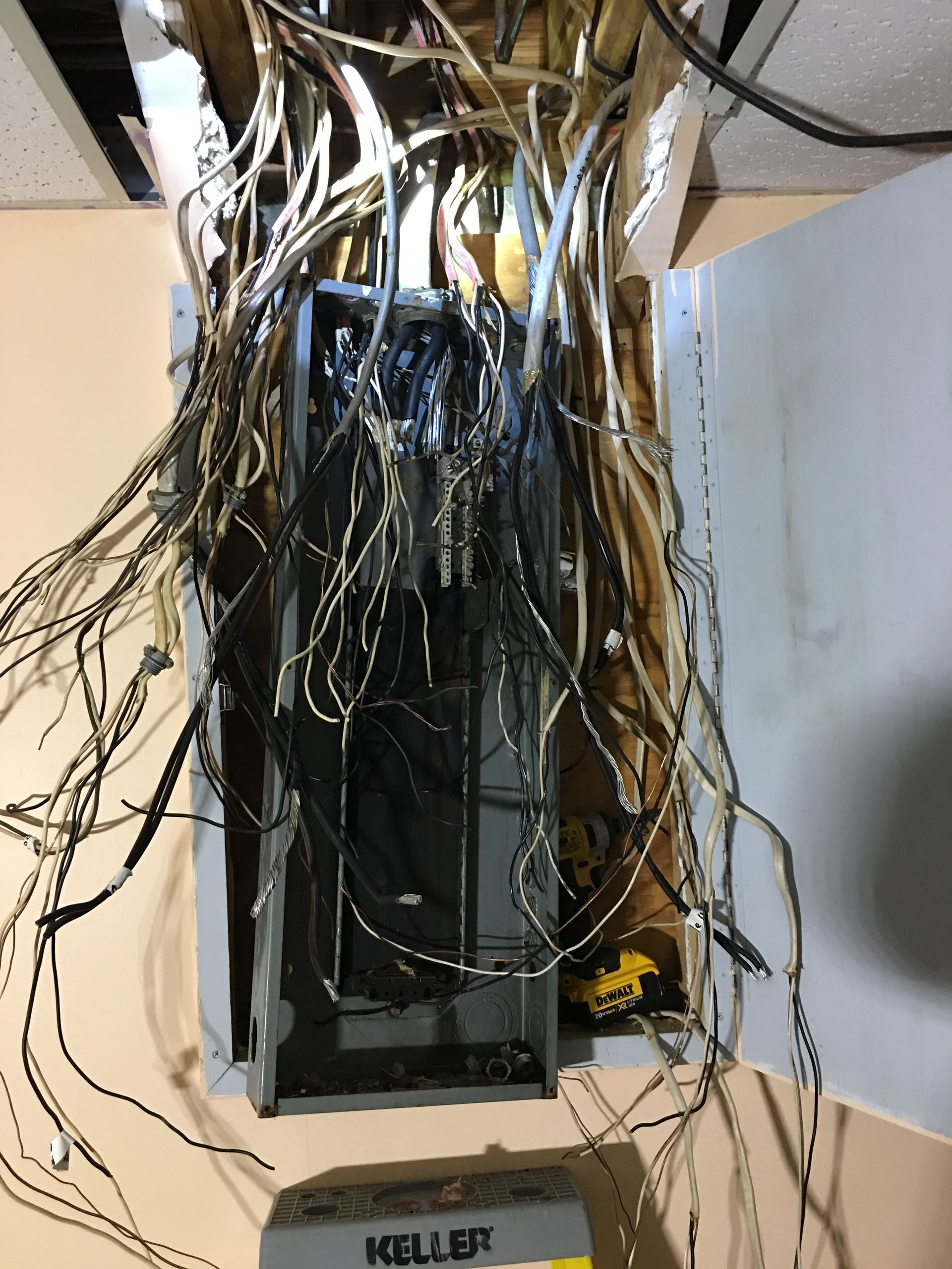 Messy bundle of exposed wires hanging from an open electrical panel in a wall cutout