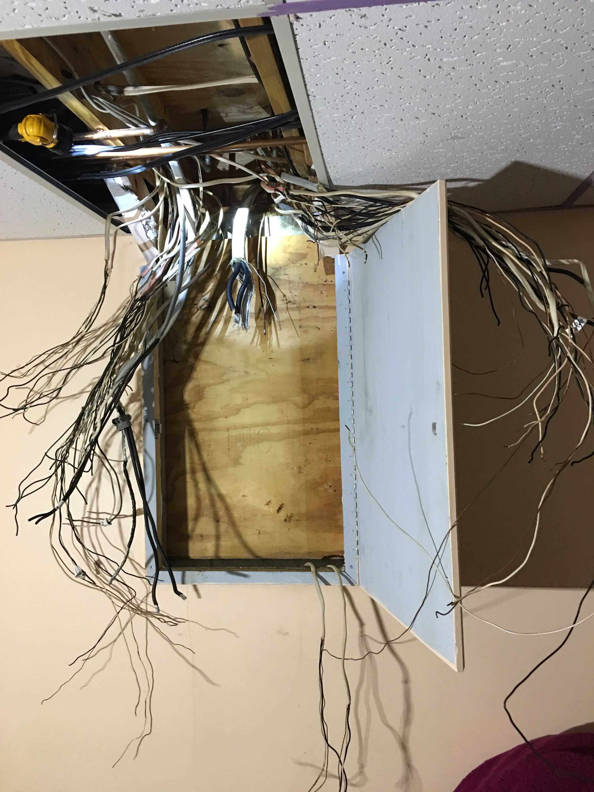 Open electrical ceiling box with exposed bundled wires and a hanging white cover panel