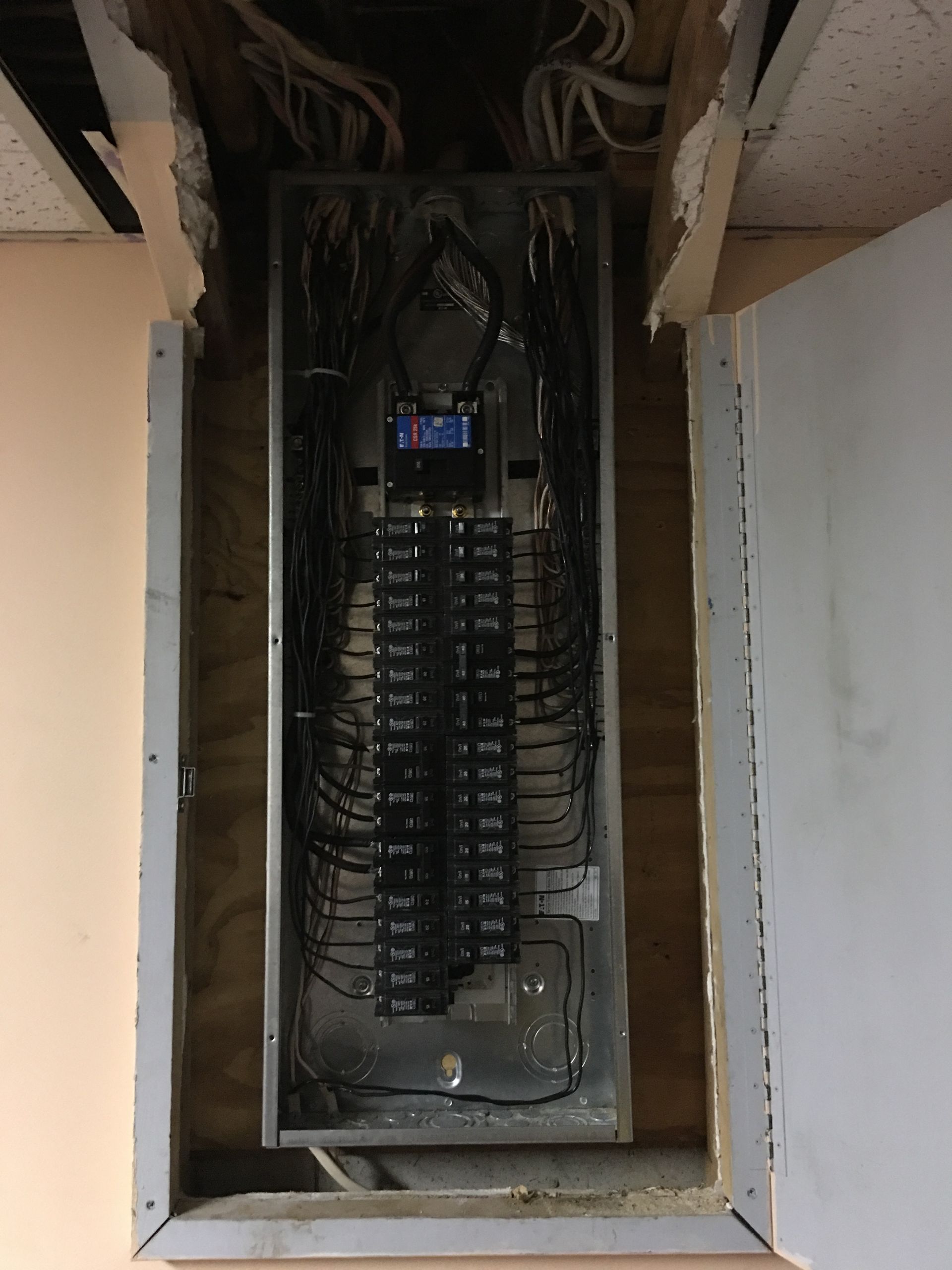 Open electrical breaker panel with multiple switches in a wall recess, wires visible above.