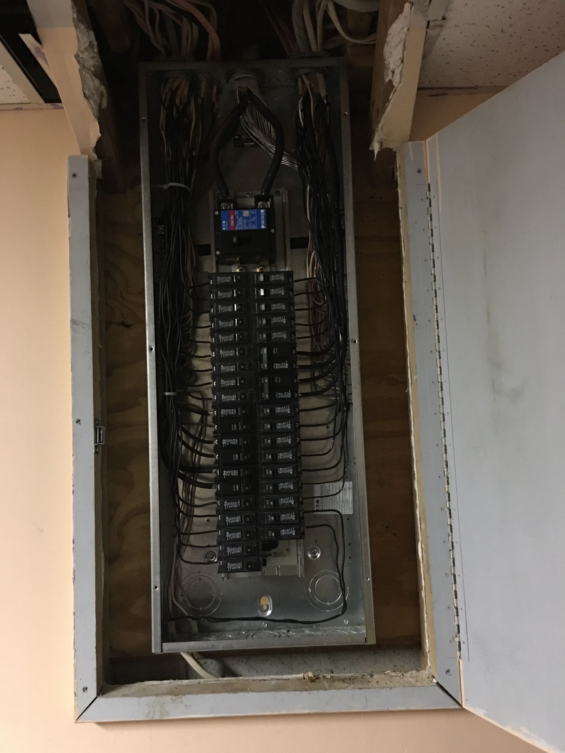 Open electrical breaker panel with rows of circuit breakers and exposed wiring in a wall recess