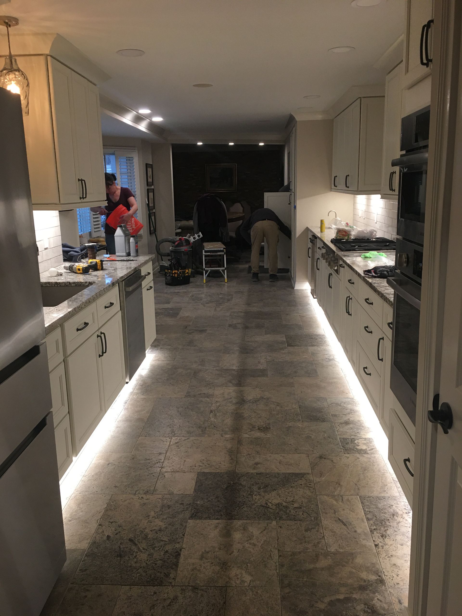 Narrow kitchen hallway with white cabinets and under-cabinet lights leading to a dark dining area