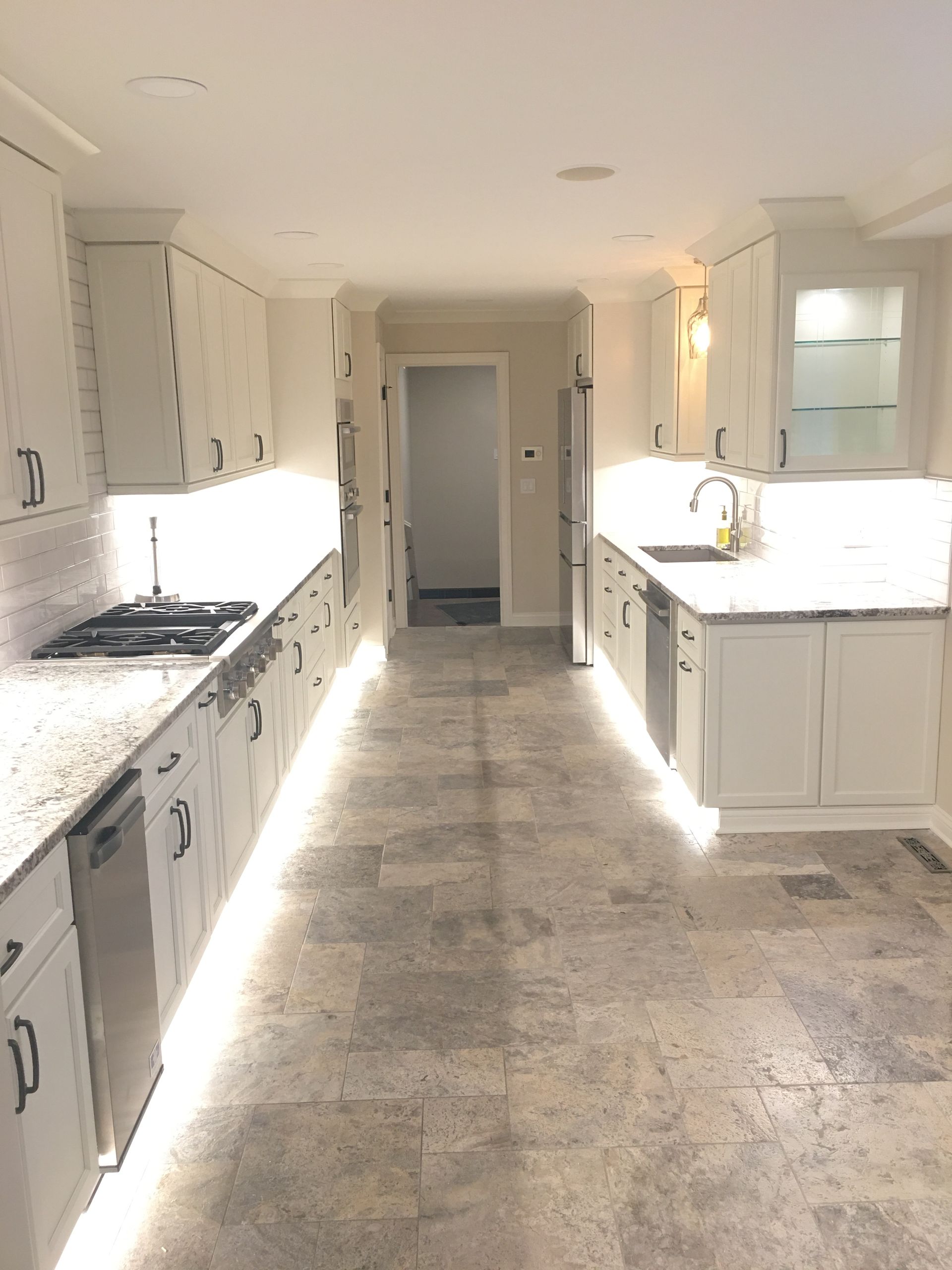 Bright white kitchen with stone counters, island sink, and a long central walkway.