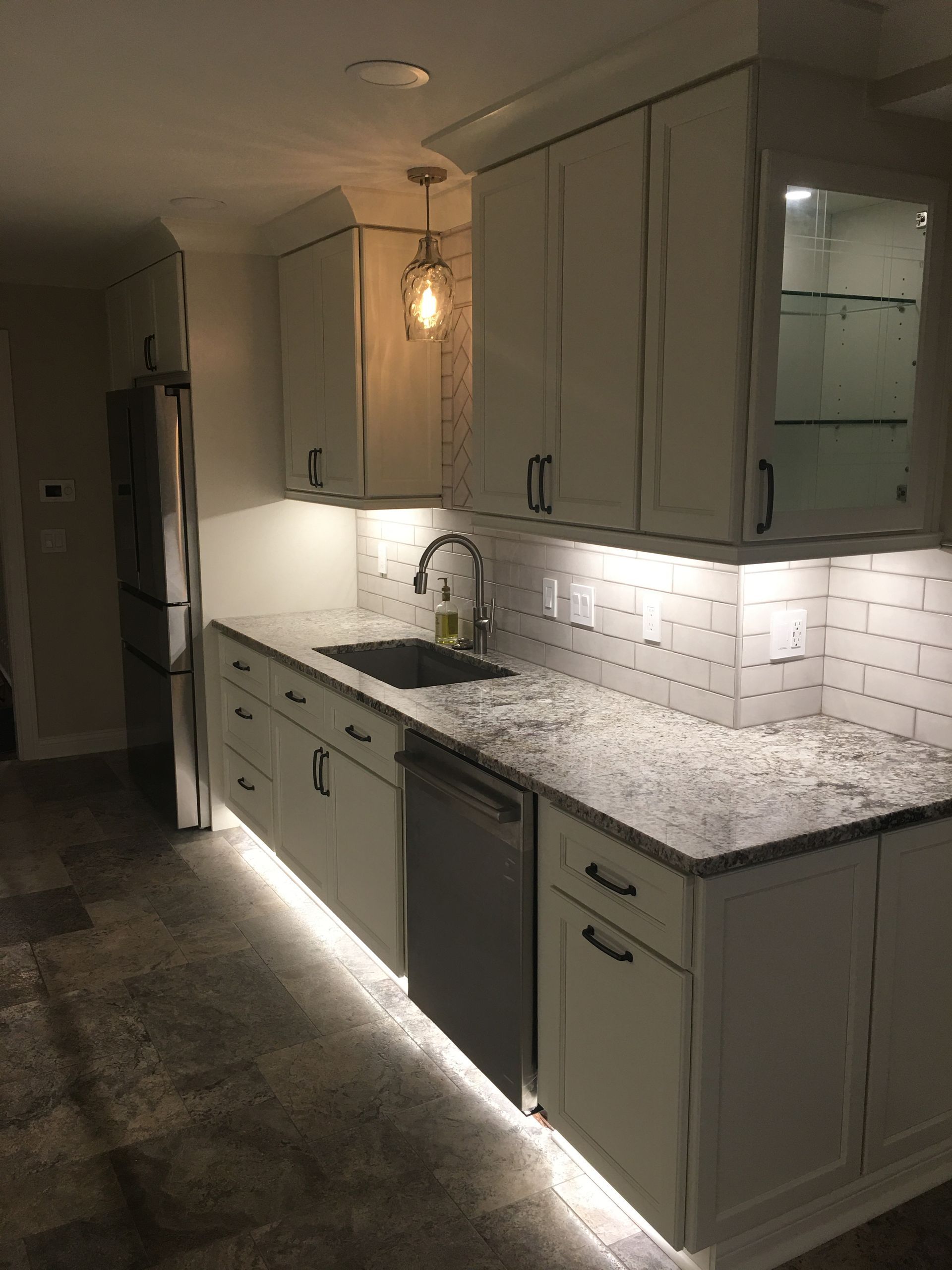 Dimly lit kitchen with white cabinets, granite countertops, and under-cabinet lighting along a dark hallway.