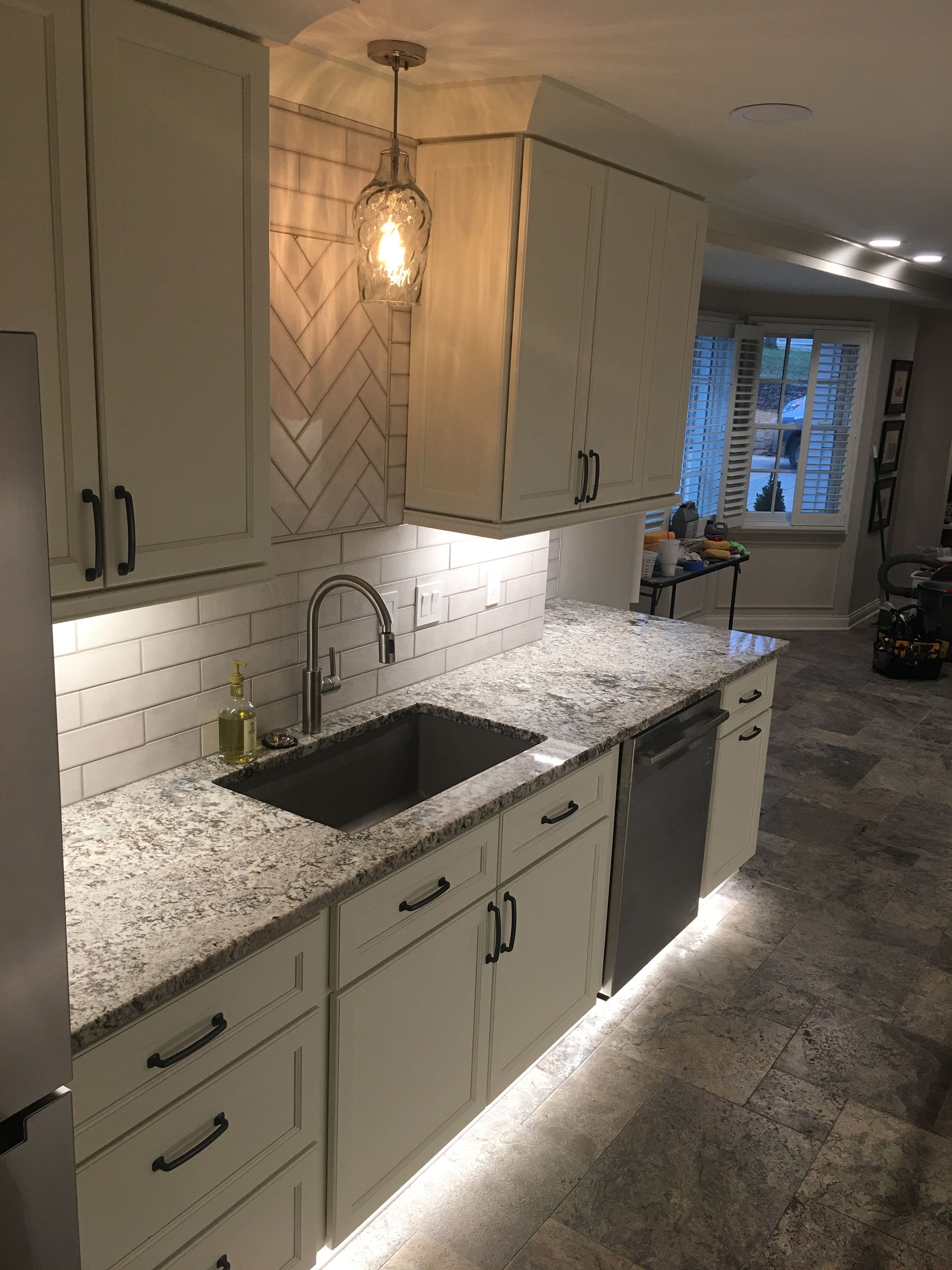 Modern kitchen with cream cabinets, granite counters, under-cabinet lighting, and a pendant light over the sink.