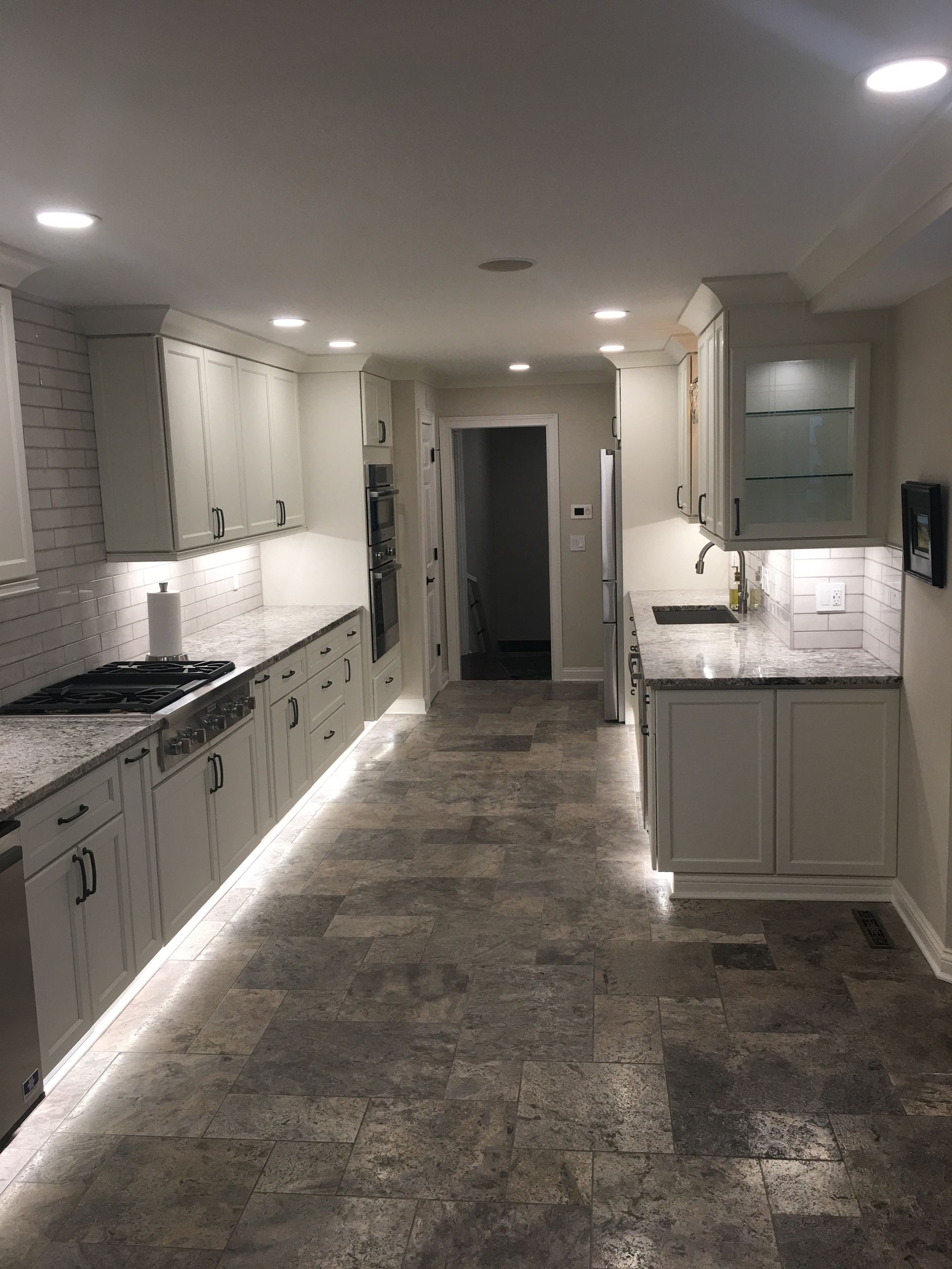 Modern kitchen hallway with white cabinets, stone counters, and gray tile flooring under recessed lights