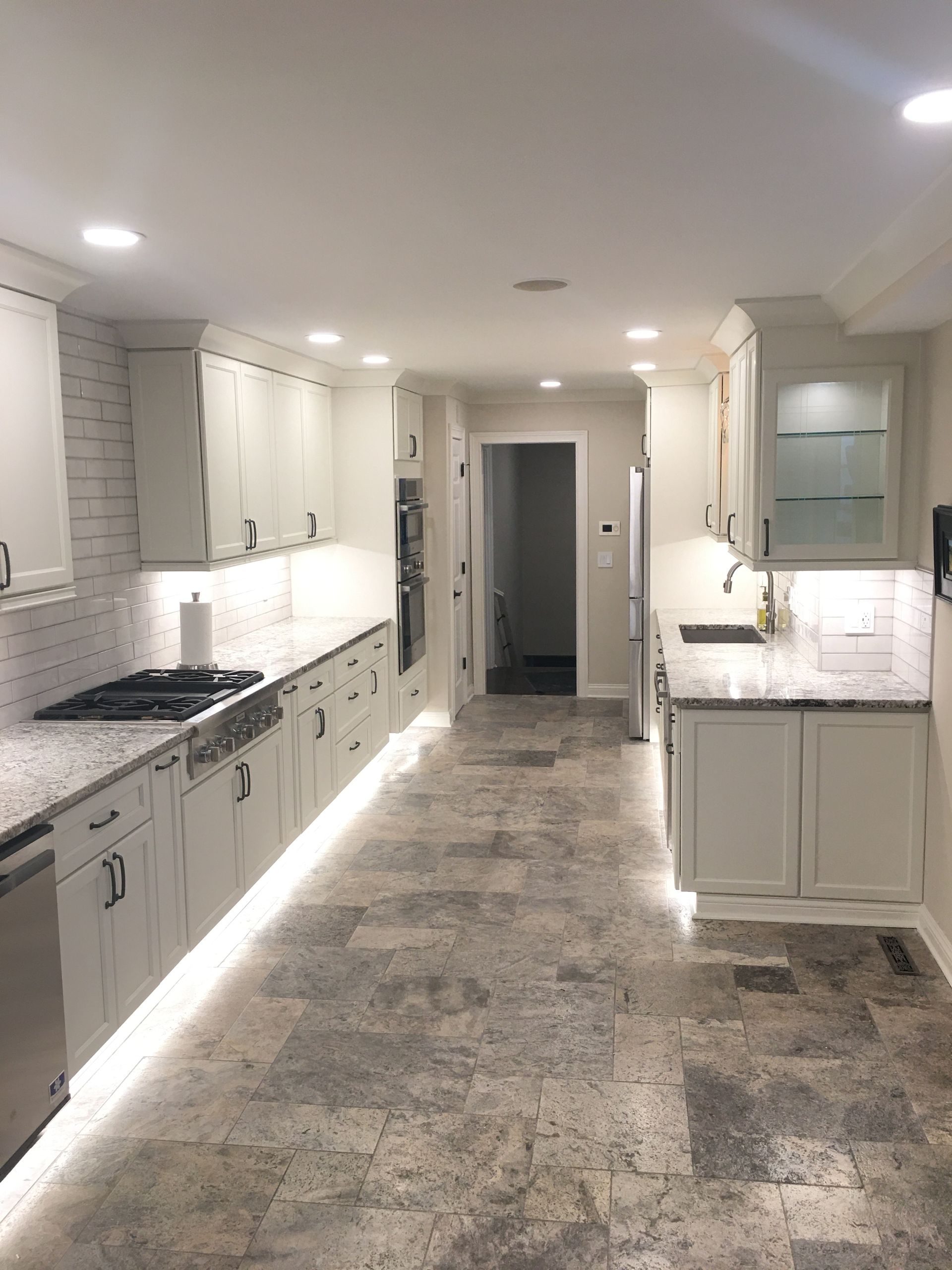 Bright white galley kitchen with light cabinets, marble countertops, and gray stone tile floor.