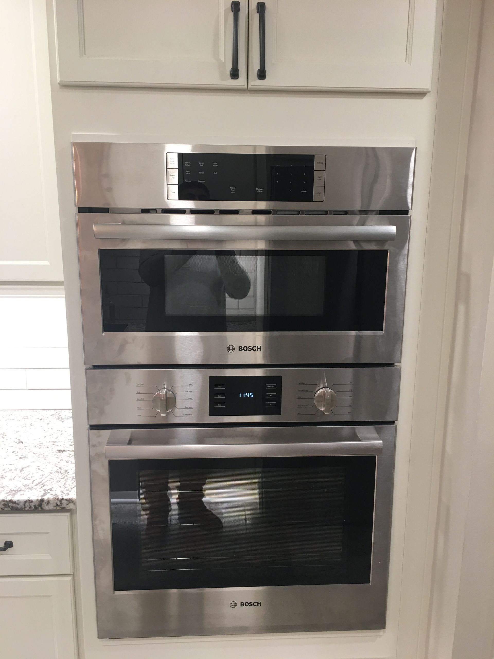 Stacked stainless steel wall ovens in a white kitchen cabinet area.