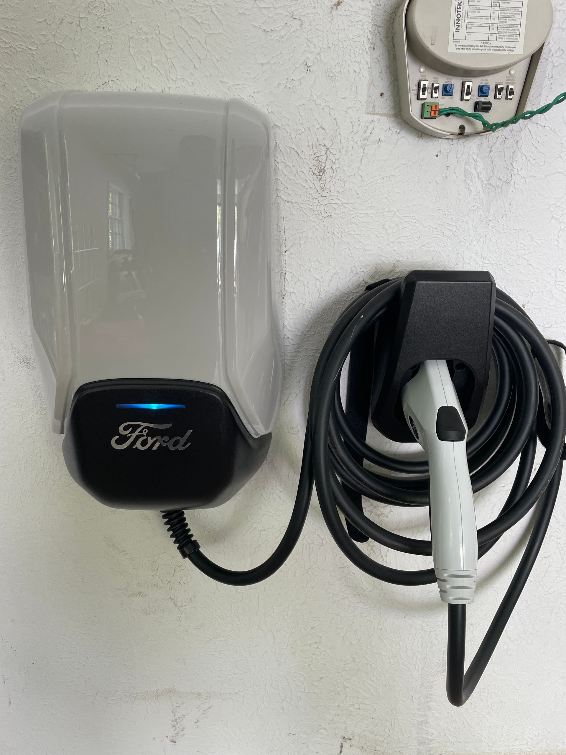 Ford electric vehicle charging connector mounted on a wall, with coiled cable on a white surface.