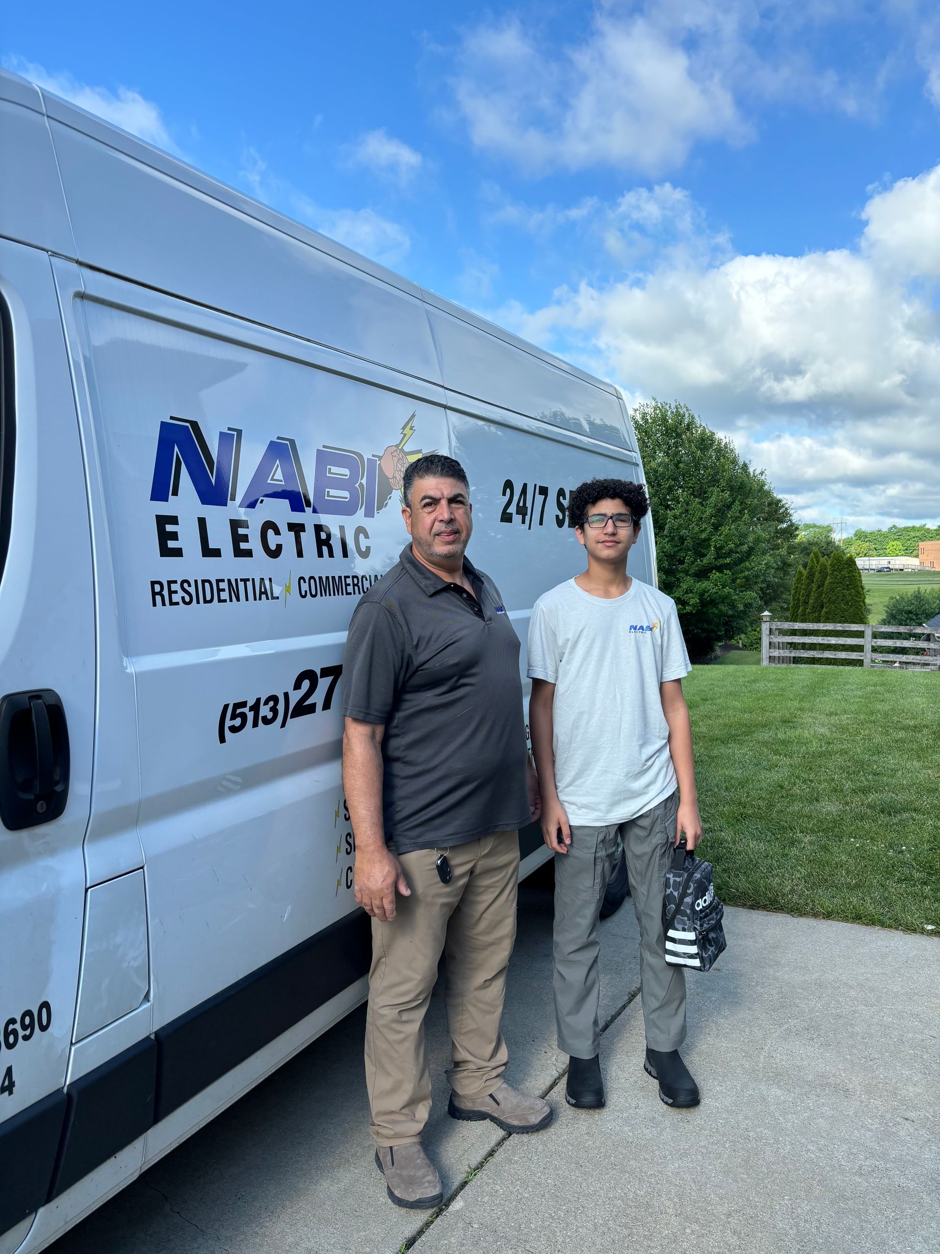 Two men standing beside a white electrical service van on a sunny day
