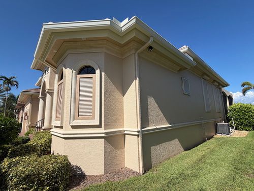 Beige stucco house exterior with shuttered windows and a grassy yard under a clear sky