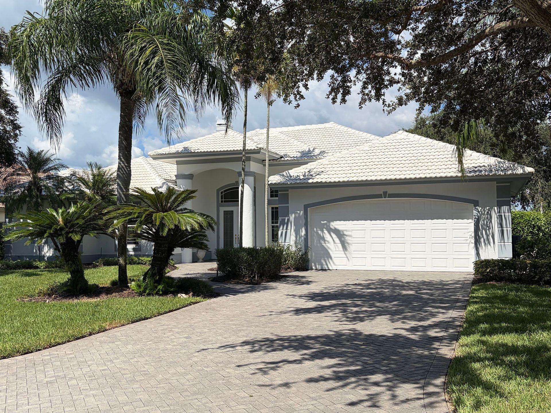 Single-story white house with a two-car garage and palm trees along a sunny driveway